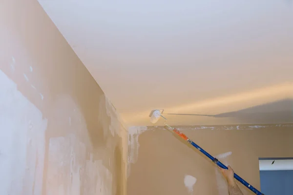 Interior reconstruction works for worker priming with a paint roller with repair the ceiling wall after applying plaster of the house room