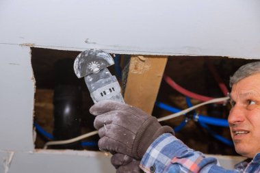 İnşaat elektrikli aletleriyle alçı tahtayı kesen işçinin hasar gören alçıpanı yerine ev yenileme servisi onarım çalışmaları