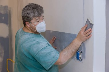 Müteahhit, oda tadilatı sırasında alçı tahta alçıpan zımparalamak için kum malası kullanıyor.