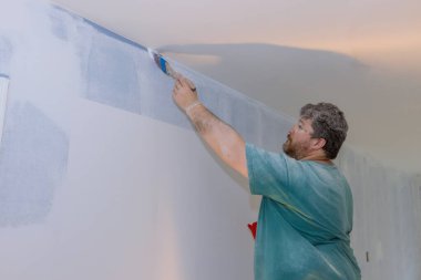 Profesyonel ressam, duvara boya sürmek için fırça kullanıyor.