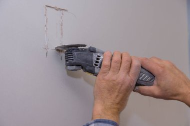Alçıtaşı alçıpan kesme delikleri üzerinde duvar lambası elektrikçisi için elektrikli aletler kullanan bir adam.