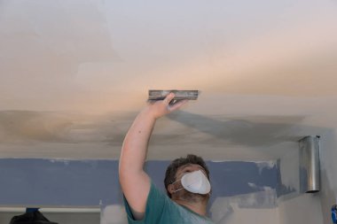 Müteahhit, odanın tadilatı sırasında tavandaki alçıpanı zımparalıyor.