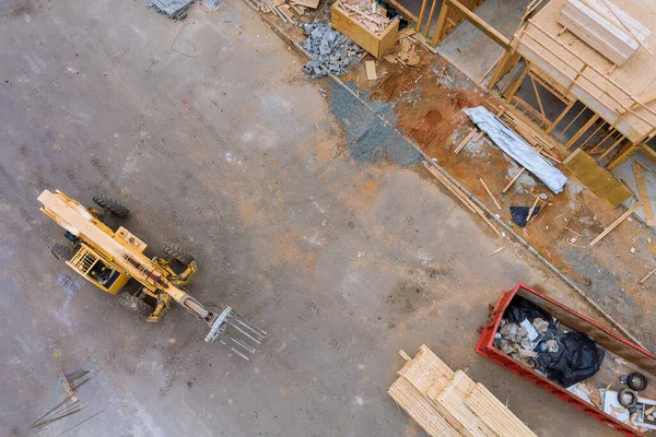 Aerial view of forklift stacker wooden boards and trash dumpsters construction on apartment beams framing of a new house under construction