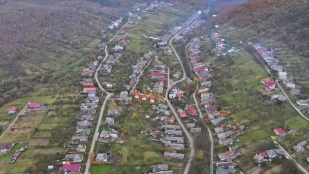 Вид с воздуха на сельскую местность с домиками между осенними горными холмами, покрытыми желтым лесом. — стоковое видео
