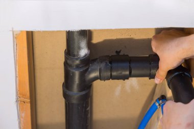 Tesisatçı, inşaat halindeki bir evin PVC kanalizasyon borularını yapıştırıyor.