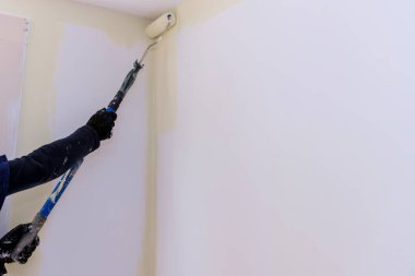 Uzun saplı boya fırçası, duvarlara beyaz astar boya uyguluyor.