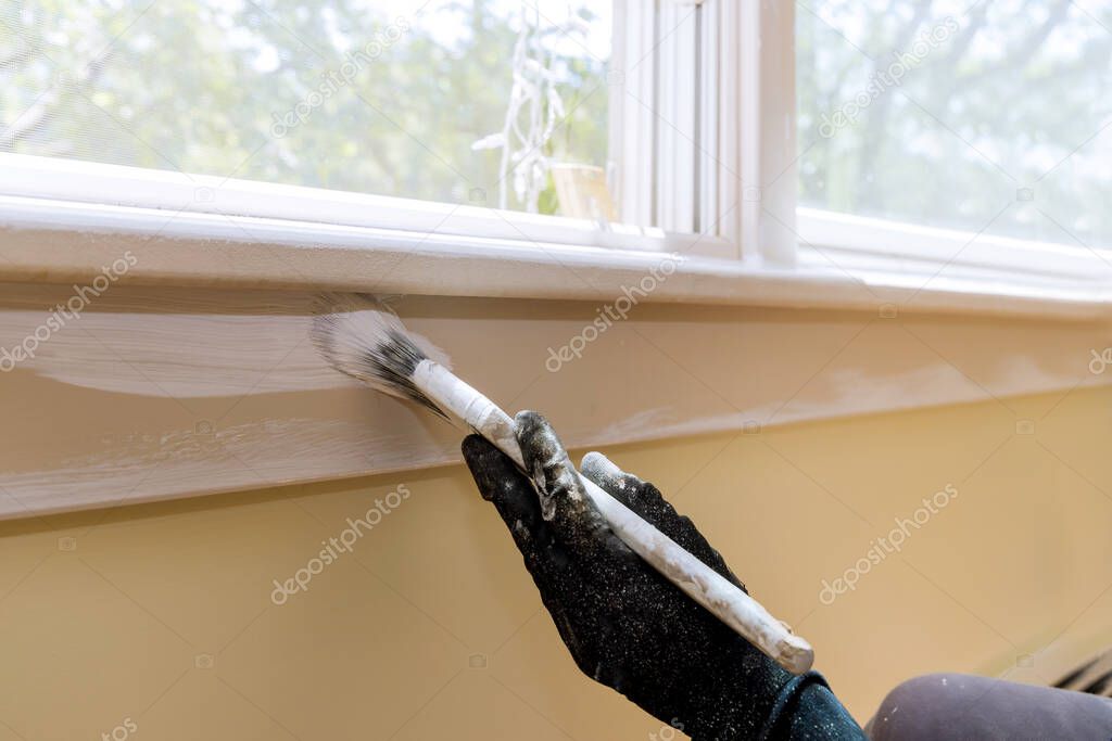 Hand of repairman painting with gloves in the painting window molding trim