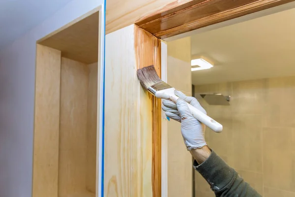 Hand of repairman painting with gloves in the brush applying varnish paint wood doors molding trim with paintbrush