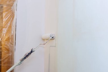 Ressamın arka görünüşü odada bir silindirle duvarı boyuyor.