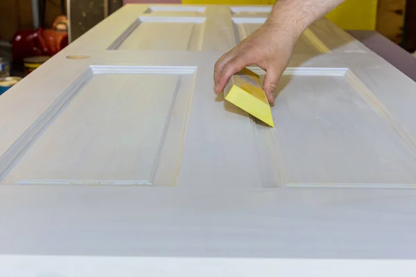 Carpenter in work on worker smooth sanding wooden interior door after primer with sanding block