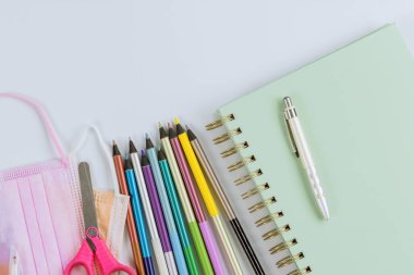 Covid-19 koronavirüsündeki tıbbi maskeler okul malzemelerinin üzerinde duran çeşitli renkli kırtasiyeler.