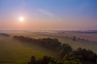 Güneş ışığı dramatik sahnesinde taze çimlerle birlikte fantastik sisli havada ılık gün doğumunun görüntüsü.
