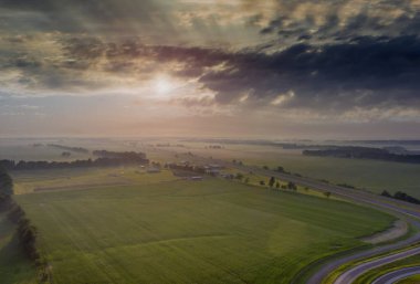 Yüksek hız otoyolu boyunca uzanan bir tarlada gün doğumu yaz mevsimi sisli ve bulutlu sabah hava manzaralı.