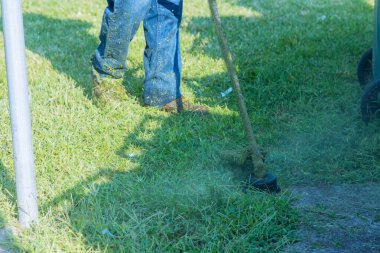 Çimenli yeşil bir çimenlikte çim biçen bir kamu görevlisi.