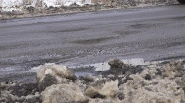 Bulutlu gri hava yolundaki kışın manzarası, arabanın sürücüsü için çukurlardaki çatlaklarla kaplıdır.