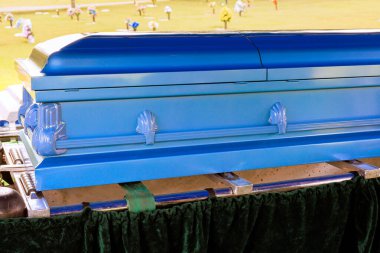 Çiçeklerle çevrili bir tabut. Huzurlu mezarlıktaki anma törenine katılanlar.