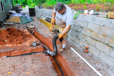 Adam evin yanındaki hendekte dururken drenaj borusunu bağlamak için özenle çalışıyor..