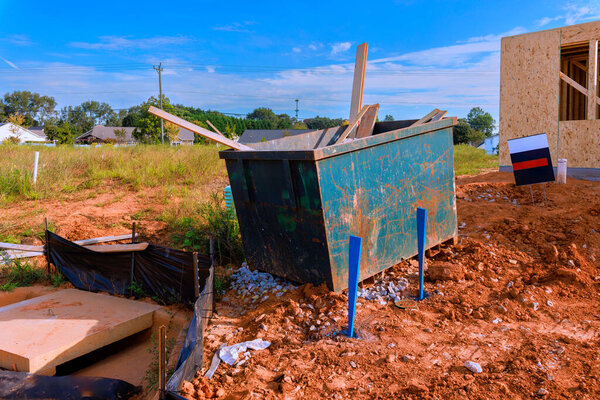 Контейнер для мусора находится на строительной площадке, окруженной строительными материалами, работающими ежедневно