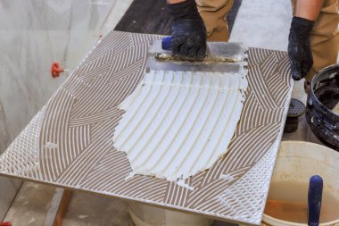 İşçi inşaat sahasına yerleştirilmeye hazır büyük fayanslara yapıştırıcı sürmek için mala kullanır.