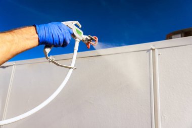 İnşaatçı inşaat sırasında duvara boya sürmek için sprey tabanca kullanıyor..