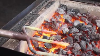 Demirci koruyucu eldiven giyerken ısıtılmış metali bahçe çatalına dönüştürmek için çekiç kullanıyor..