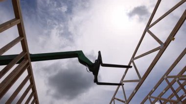 İnşaat alanındaki telgraf makinesi ahşap kirişi kaldırıyor ve tepesinde bulutlar var..