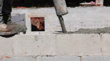 İnşaat işçisi tuğla duvarın üzerinde duruyor, inşaat alanındaki boşluklara taze beton döküyor..