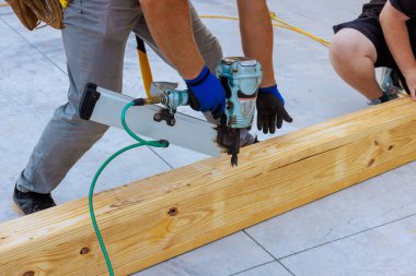 İnşaat alanında tahta kirişleri hava çivi tabancasıyla güvenceye alan iki işçi.