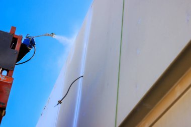 İşçi, kaldırma ekipmanında yükselirken bina duvarına sprey boya uygular