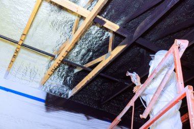 Merdivendeki işçiler yenileme sırasında ahşap kirişlere köpük yalıtımı üzerine siyah boya püskürtüyorlar..