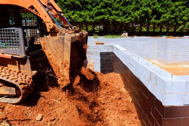 İnşaat işçisi, inşaat temeline toprak yüklemek için kazıcı kullanıyor