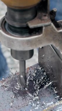 İşçi, metal kirişleri delmek ve talaş üretmek için makine çalıştırıyor