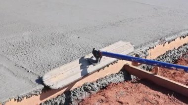 İnşaat işçisi inşaat alanındaki ıslak betonu yumuşatmak için seviyelendirme aracı kullanıyor