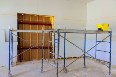 İnşaat iskelesi, tamamlanmamış duvar inşaatı aletleriyle tadilat yapılan bir odada duruyor.