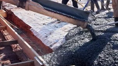 İşçiler inşaat alanında ahşap formları betonla dolduruyorlar.
