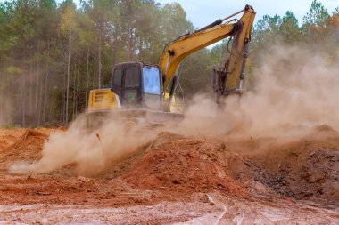 Kazı makineleri inşaat alanında toprağı kazarak ağaçların arasına toz bırakıyor..