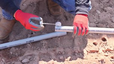 Eldiven giyen işçiler yerdeki sulama sistemi için PVC boru bölümlerini birleştiriyorlar..