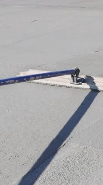 Çimento işçisi inşaat alanındaki ıslak betonu düzleştirmek için uzun bir alet kullanıyor.
