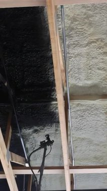 Merdivendeki işçiler yenileme sırasında ahşap kirişlere köpük yalıtımı üzerine siyah boya püskürtüyorlar..