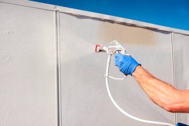 Eldivenli tamirci, iş gününün altındaki duvarı boyamak için sprey tabanca kullanıyor.