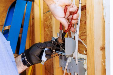 Elektrik işçisi inşaat halindeki merdivenin üzerinde dururken elektrik kablolarını bağlıyor.