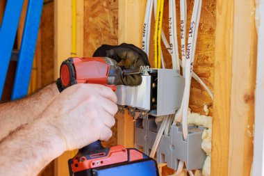 Yetenekli elektrikçi yeni inşa edilmiş yapıya bağlantı kutusu yerleştirirken elektrik kablolarını bağlıyor.