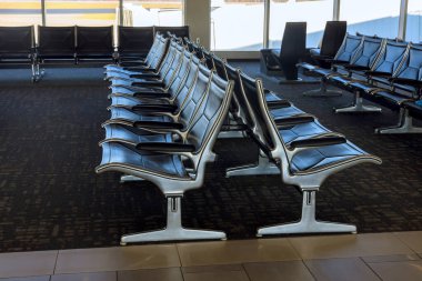 Sıralar dolusu boş deri koltuklar, parlak havaalanı bekleme alanını dolduruyor. Gezginleri dinlenmeye davet ediyor..