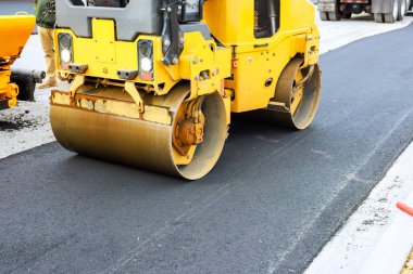 Ağır patenler inşaat halindeki yolda yeni yerleştirilmiş asfaltı sıkıştırıyor