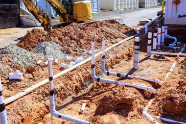 İşçiler kanalizasyon sistemi için inşaat alanındaki siperlere boru döşüyorlar.