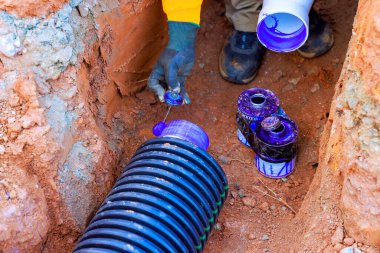 İşçi, yerleşim için alet konteynırları kullanarak, toprakla dolu bir sipere drenaj borusu yerleştiriyor..