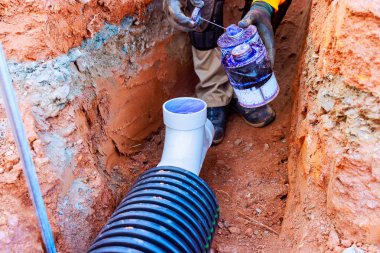 Eldiven işçisi inşaat alanında kurulum sırasında drenaj borusuna dolgu maddesi uyguluyor