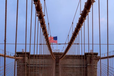 Brooklyn Köprüsü 'nde yürürken Amerikan bayrağı dalgalanırken New York şehrinde Amerikan tarihi simgesinde ufuk çizgisinde
