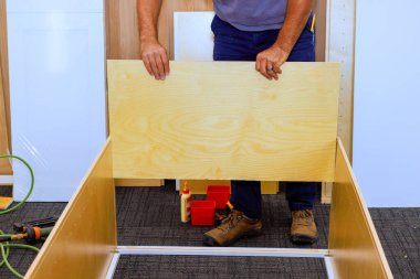 Müteahhit, çalışma alanındaki aletleri, vidaları, tahtaları kullanarak ahşap dolabı birleştirir