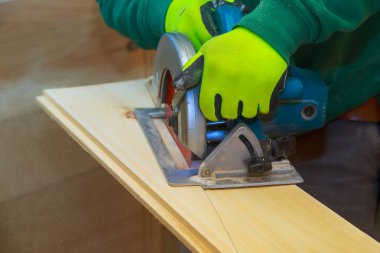 Müteahhit, atölyede tahta kesmek için testere kullanıyor. Korunmak için eldiven takıyor..